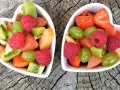 Dwa sercowate talerzyki pełne kolorowych, pokrojonych owoców: truskawek, malin, kiwi, winogron i grejpfruta. Idealne zdrowe przekąski dla dzieci.