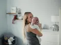 Mama tuli noworodka, kołysze go czule. Pokój dziecięcy z pluszakami i lampką w kształcie słonia.