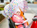 Dziecko w wózku, ubrane na 21 stopni: różowa kurtka, czapka. Gwiazdkowy daszek chroni przed słońcem.