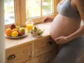 Kobieta w 39 tygodniu ciąży je sałatkę. Obok stoi talerz z owocami i sok pomarańczowy.