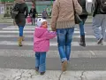 Małe dziecko w różowej kurtce i czapce z uszami idzie za rękę z dorosłym. Widać, jak ubrać niemowlę na spacer 12 stopni.