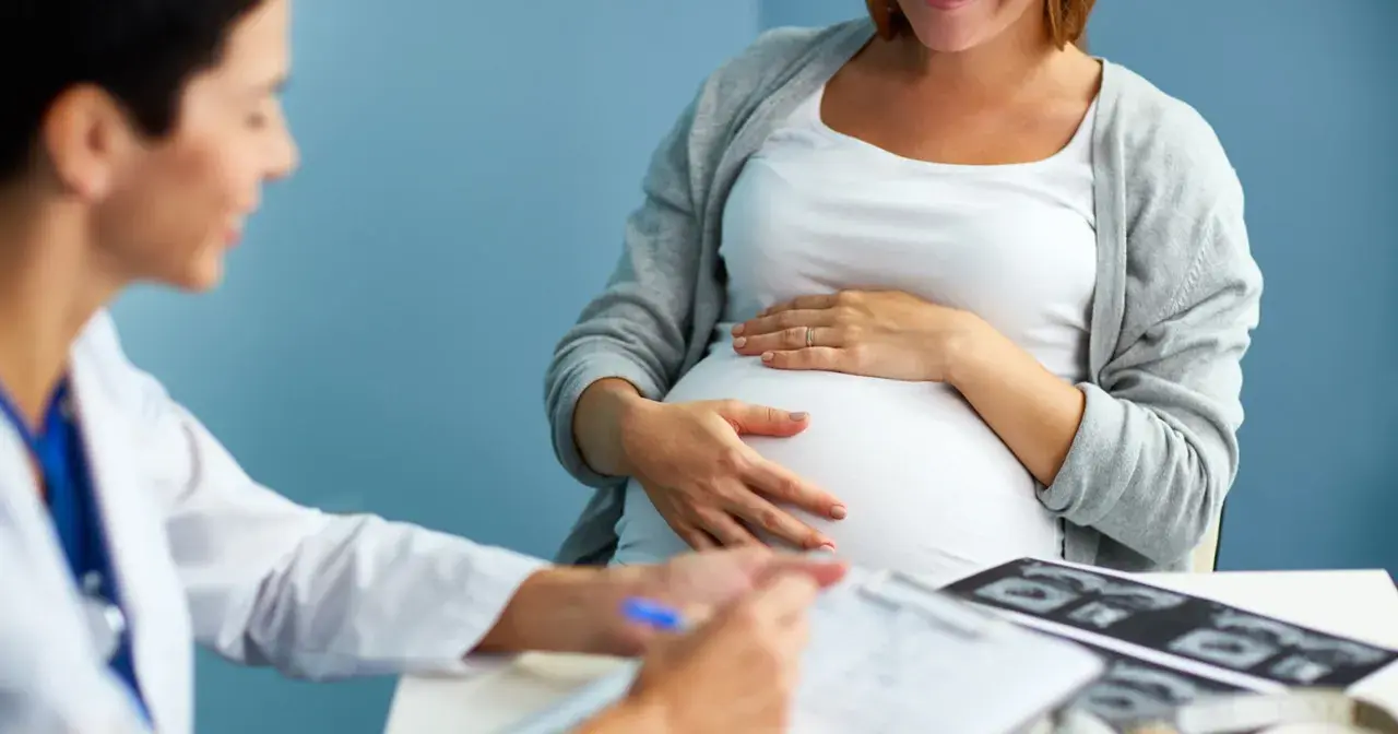 Lekarz konsultuje pacjentkę w 36 tygodniu ciąży. Na stole leżą zdjęcia USG.