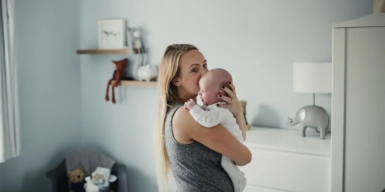 Mama tuli noworodka, kołysze go czule. Pokój dziecięcy z pluszakami i lampką w kształcie słonia.
