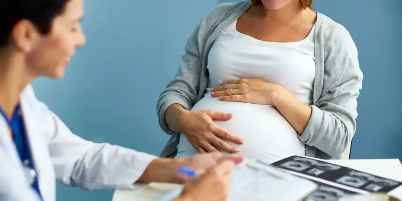 Lekarz konsultuje pacjentkę w 36 tygodniu ciąży. Na stole leżą zdjęcia USG.