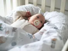 Malutkie dziecko w łóżeczku z uspokajającym smoczkiem w kształcie sutka.