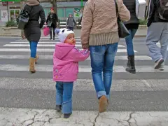 Małe dziecko w różowej kurtce i czapce z uszami idzie za rękę z dorosłym. Widać, jak ubrać niemowlę na spacer 12 stopni.