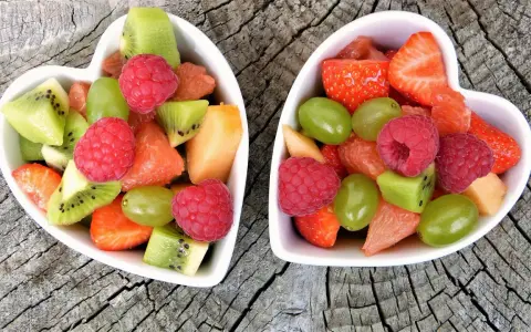 Dwa sercowate talerzyki pełne kolorowych, pokrojonych owoców: truskawek, malin, kiwi, winogron i grejpfruta. Idealne zdrowe przekąski dla dzieci.