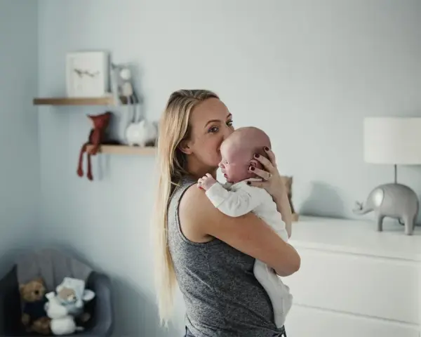 Mama tuli noworodka, kołysze go czule. Pokój dziecięcy z pluszakami i lampką w kształcie słonia.