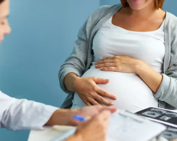 Lekarz konsultuje pacjentkę w 36 tygodniu ciąży. Na stole leżą zdjęcia USG.