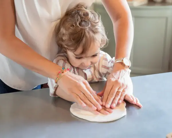 Ręce mamy i dziecka lepią ciasto. Piękna chwila dla przyszłej mamy, która już teraz uczy się wspólnego gotowania.