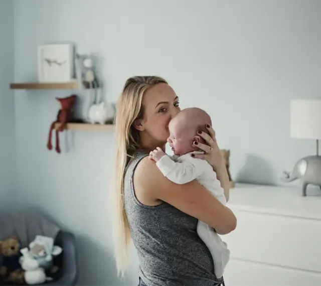 Mama tuli noworodka, kołysze go czule. Pokój dziecięcy z pluszakami i lampką w kształcie słonia.