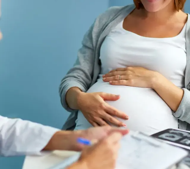 Lekarz konsultuje pacjentkę w 36 tygodniu ciąży. Na stole leżą zdjęcia USG.