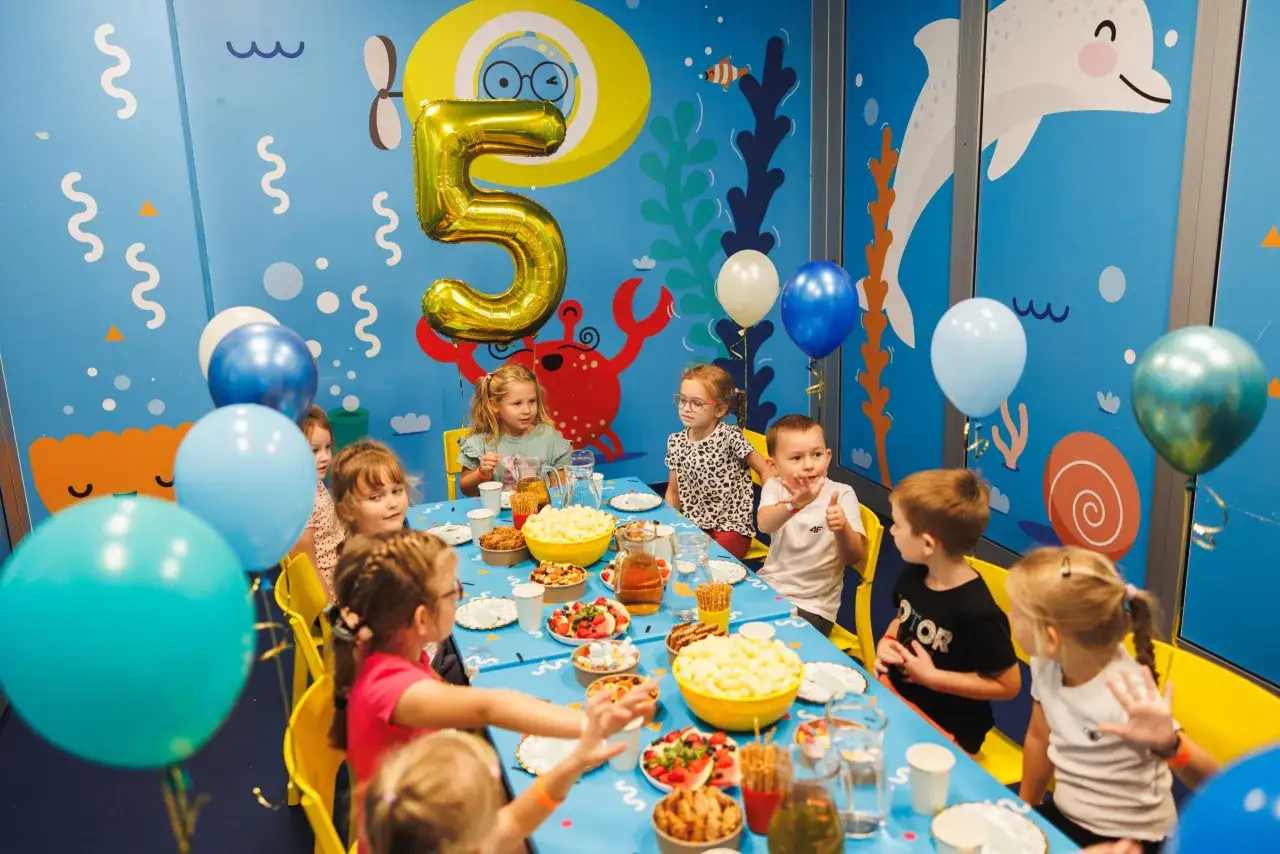 Dzieci świętują 5 urodziny przy stole pełnym przekąsek, otoczone balonami i morskimi dekoracjami.
