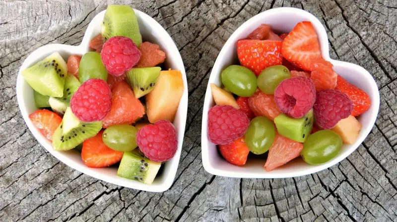 Dwa sercowate talerzyki pełne kolorowych, pokrojonych owoców: truskawek, malin, kiwi, winogron i grejpfruta. Idealne zdrowe przekąski dla dzieci.