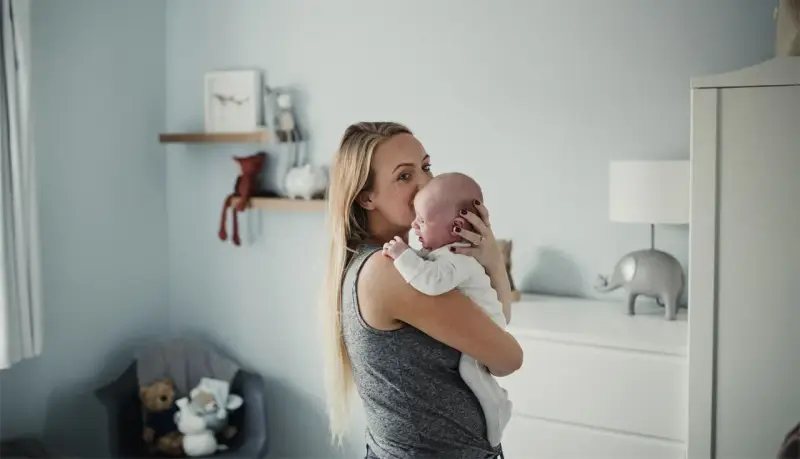 Mama tuli noworodka, kołysze go czule. Pokój dziecięcy z pluszakami i lampką w kształcie słonia.